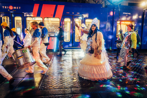 Performers march in the Lantern Procession past a TriMet MAX train at the Portland Winter Light Festival