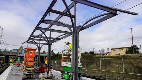A worker in a fluorescent safety vest operates a scissor lift during construction at the NE 82nd Ave MAX Station in Portland