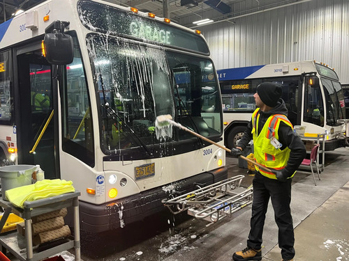 A worker in a safety vest washes the windshield of bus 3004 at a TriMet maintenance facility