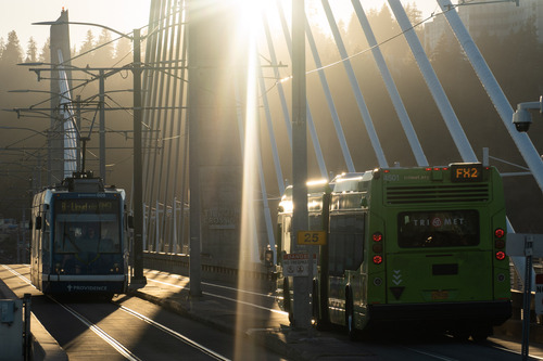 A TriMet FX bus and Portland Streetcar cross Tilikum Crossing in warm light