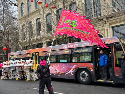 Dragon dancers and a person waving a flag in front of TriMet's special bus commemorating Asian American and Pacific Islander Heritage Month.