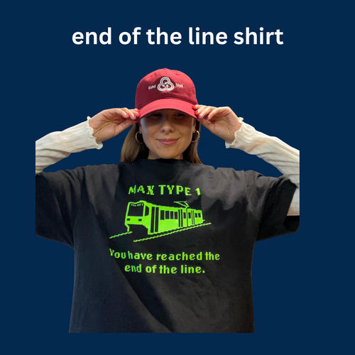 Person adjusting a TriMet logo hat, wearing a black “end of the line” trainT-shirt with neon green font