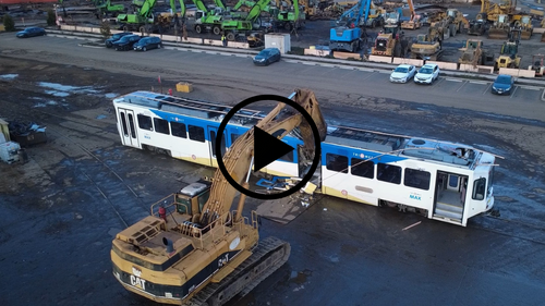 An excavator is tearing apart a light rail train in an industrial yard