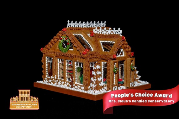 photo of a brown gingerbread house decorated with white piping, wreaths and red accent decorations