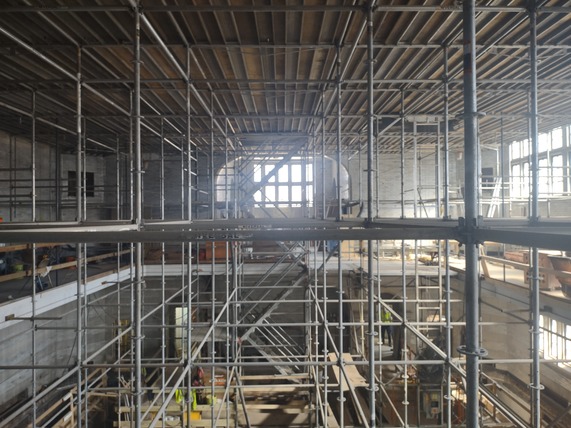 Inside a building with wood covering the floors and scaffolding going up 6 stories to the bare ceiling slats