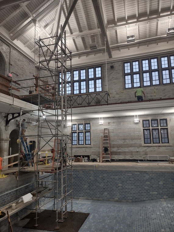 Interior of a pool house building with a pool tiled in blue and scaffolding in the left of the pool going up towards the ceiling