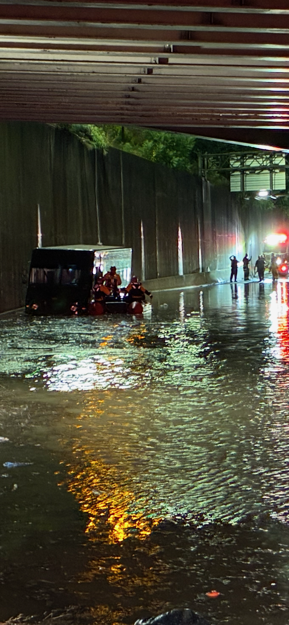 Photo of a truck in deep water under and underpass with a boat with firefighters alongside