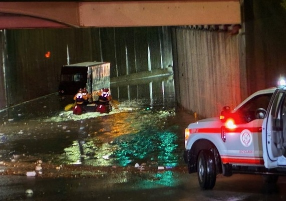 Photo of a flooded underpass with a boat of rowers with high-visibility vests going towards a trapped UPS truck