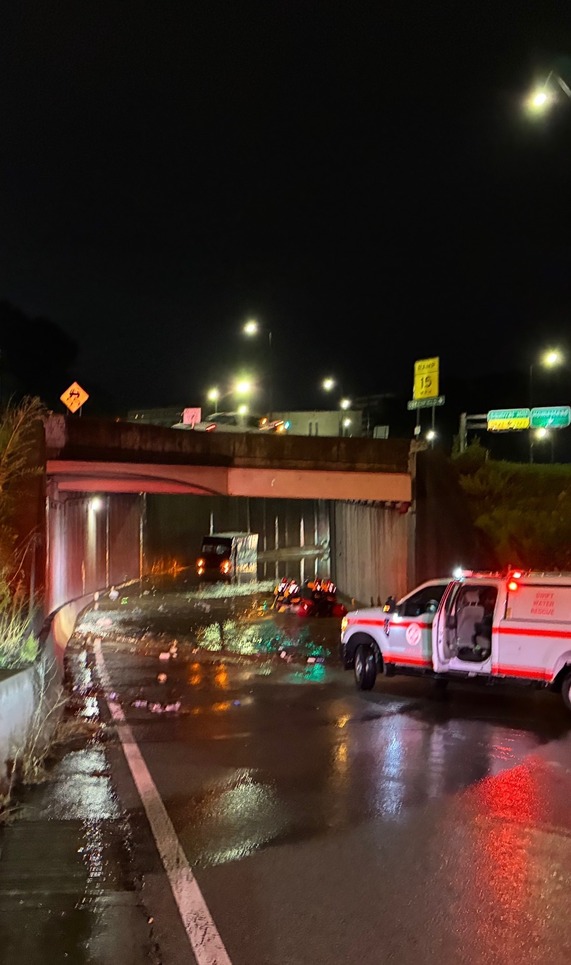 Photo of a fire vehicle near a flooded overpass with a boat of rowers in hi-visibility vests moving towards a trapped UPS truck