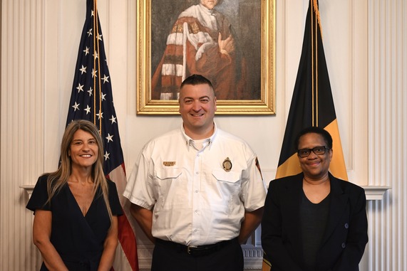 3 people by American and Pittsburgh flags: a woman with long blonde hair, a man with short dark hair, a woman with short dark hair and glasses