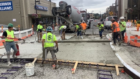 Several construction workers use concrete finish equipment to spread out concrete mixture.