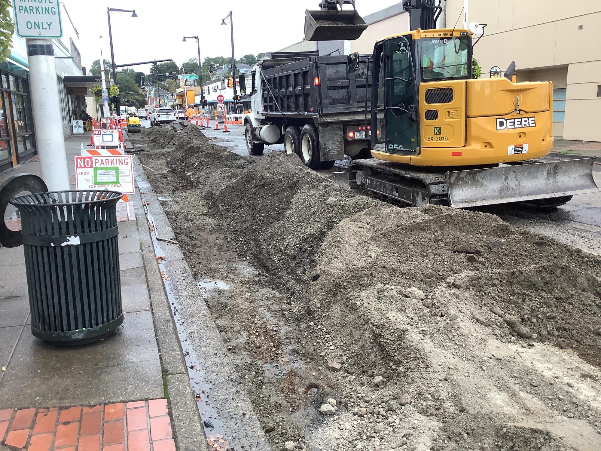 Crews use heavy equipment to add gravel and compact it in the curbside parking  