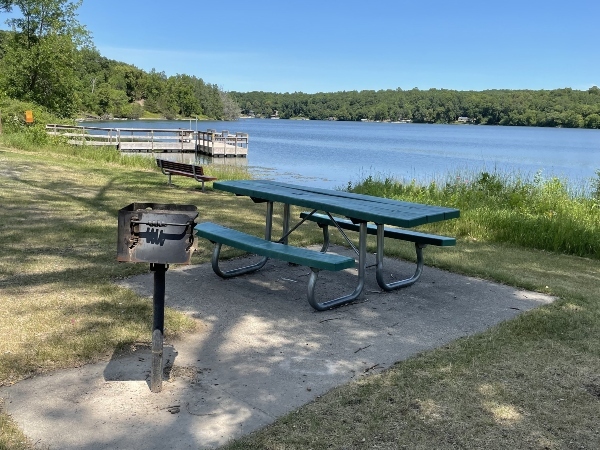 grill by picnic table with fishing pier and lake in background