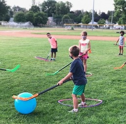 Youth wearing cloth masks playing field hockey.