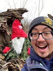 Man taking a selfie with a spruce bough "tree gnome" in a Saint Paul park. 