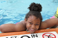 Youth swimmer smiling for the camera at the edge of a swimming pool. 