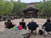 Four people sit in lawn chairs facing a Music in the Parks concert in Mears Park. 