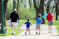 Family of 4 walking through a park with trash bags to pick up garbage