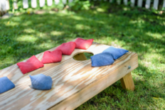 Cornhole board on grass with blue and red sand bags 