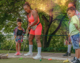 A family dressed in bright neon clothing plays mini golf outdoors at the Como Park mini golf course. 