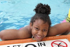 Youth smiling and holding onto the edge of a pool deck.