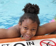 Youth smiling and holding onto the edge of a pool deck.