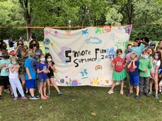 Youth wearing masks pose next to a homemade sign that reads "S'more Fun". 