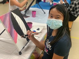 Youth wearing a mask while painting a canvas. 