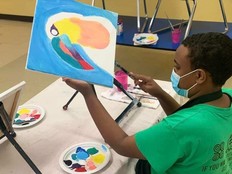 Youth in a green shirt painting a colorful toucan bird. 