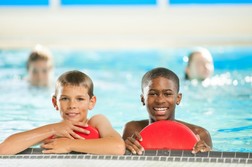 Two smiling youth holding kick boards on the edge of a pool deck. 