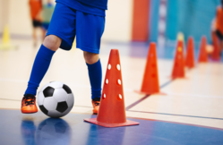 Youth in a blue uniform practicing futsal soccer around orange cones