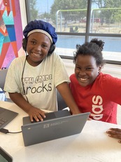 Two youth girls using a Chromebook and smiling at the camera