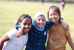 3 youth girls smiling at camera with arms around each other