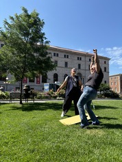 Two people playing corn hole in Rice Park_victory celebration_library in background