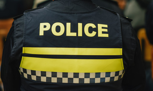 The back of a police officer with a vest that has yellow letters and spell out, POLICE. 
