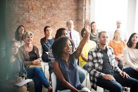 Business owners sit in a crowd listening to a speaker, one has her hand up to answer a question