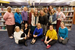 Group of Women Standing and Sitting in Front of Library Stacks
