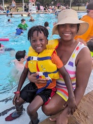 Smiling mom holding son in a lifejacket on the side of a pool