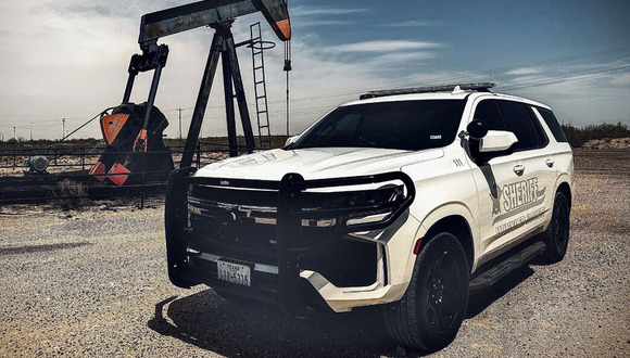 An SUV labeled county sheriff parks near a pumpjack