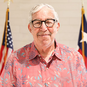 Stuart Greenfield headshot in front of United States and Texas flags