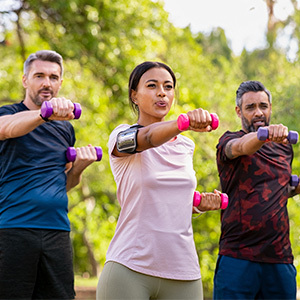 three adults exercising in a park with dumbbells