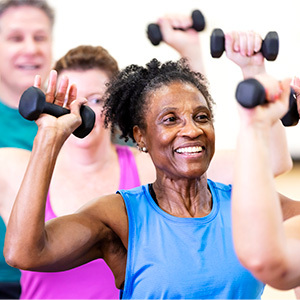 Senior woman in group exercise class sitting on fitness balls and lifting hand weights