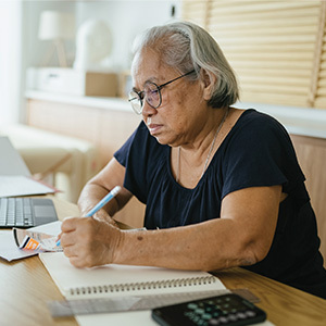 Senior woman working on finances and writing on a notepad at home