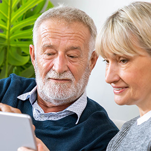 Happy senior couple sitting on couch looking at iPad