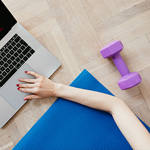 woman using weights, yoga mat and laptop