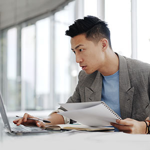 Office worker typing on laptop with papers in hand