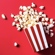 Popcorn in a striped box spilling out on to a red background