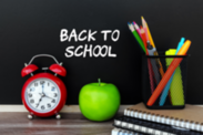 Chalkboard with the words "Back to School" on it, an alarm clock, apple, pens, pencils, and a stack of notebooks.