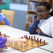 Two young girls playing a game of chess at the library