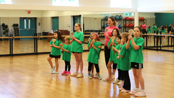 Children and Class instructor smiling wearing matching shirts in dance room